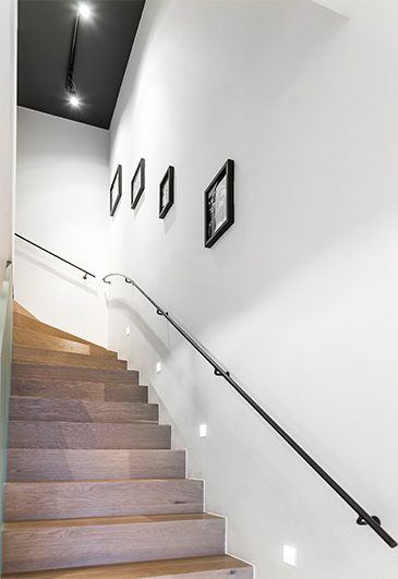 Holztreppe mit schwarzem Handlauf an weißer Wand